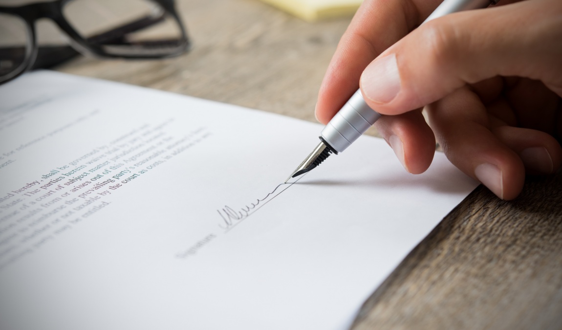 Close up of hand of businessman signing a form. Business man signing contract for future deal. Business man signing legal document. Male hand signing employee contract with a bond.